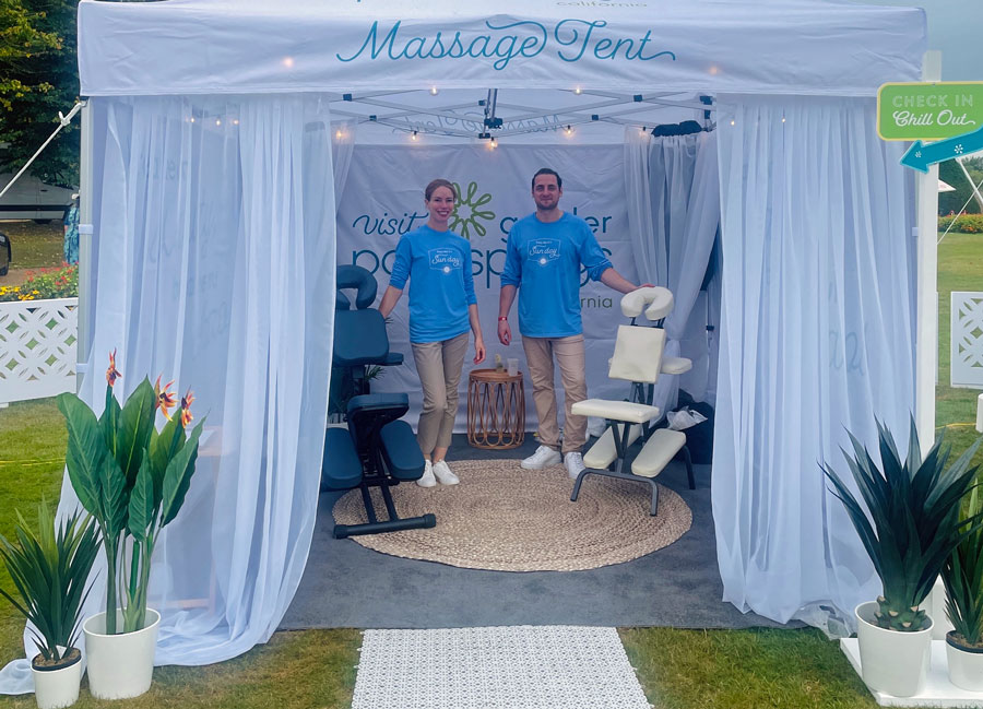 Two Sense Massage therapists standing by their massage chairs in a promotional tent